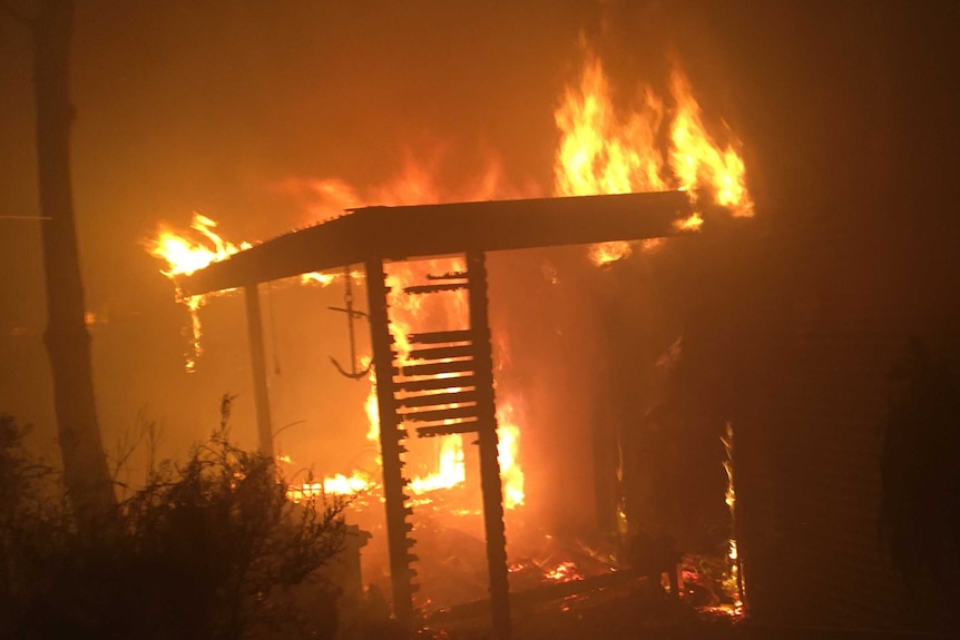 A house engulfed in flames, with wooden slats burning.