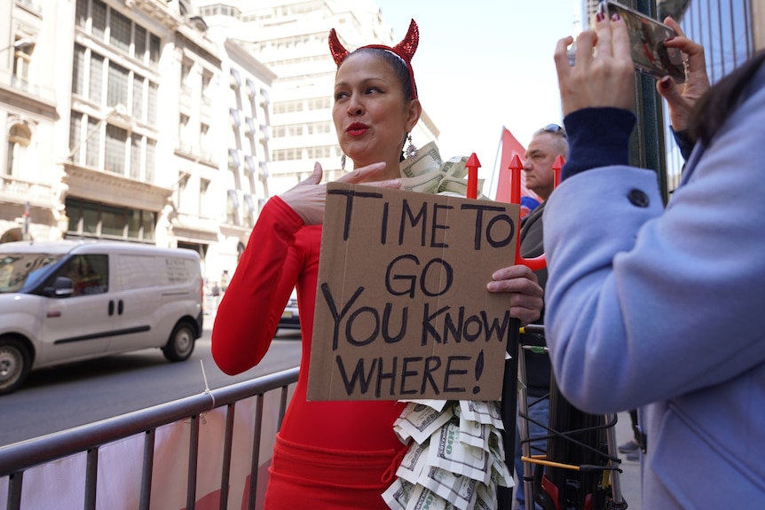 A woman appears in a devil costume with a sign.