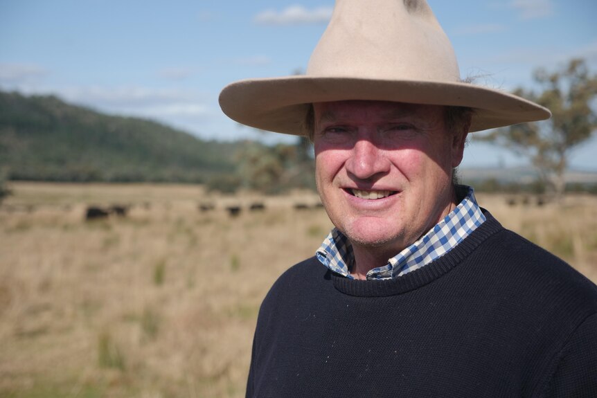 A smiling, middle-aged man in a broad-brimmed hat stands in a paddock.