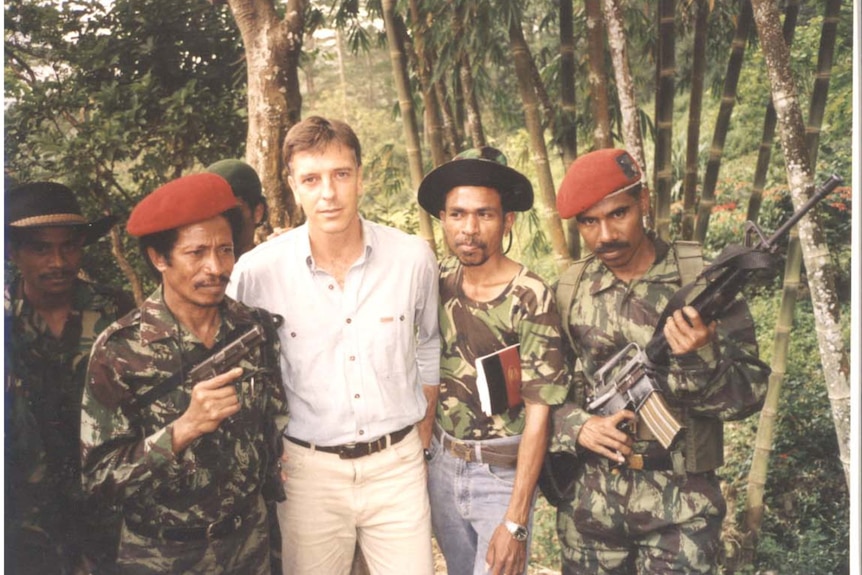 An ABC reporter standing with Timor soldiers with guns