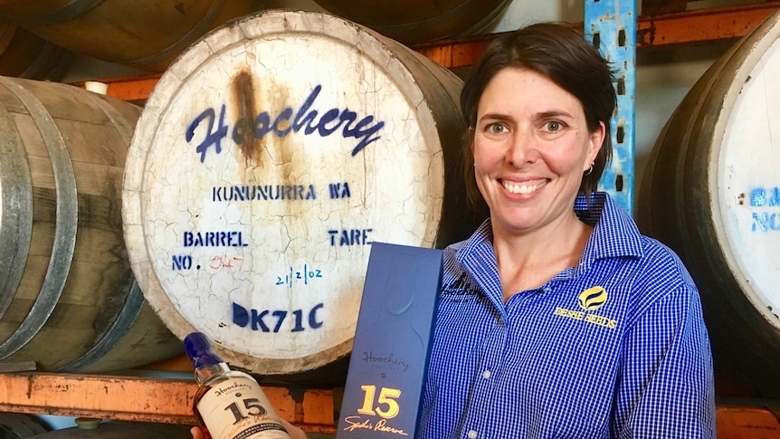 Woman holding bottle of 15 year old rum in front of wooden barrels