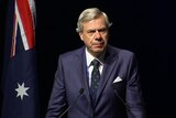 Michael Kroger standing at a lectern with the Australia flag on his left.