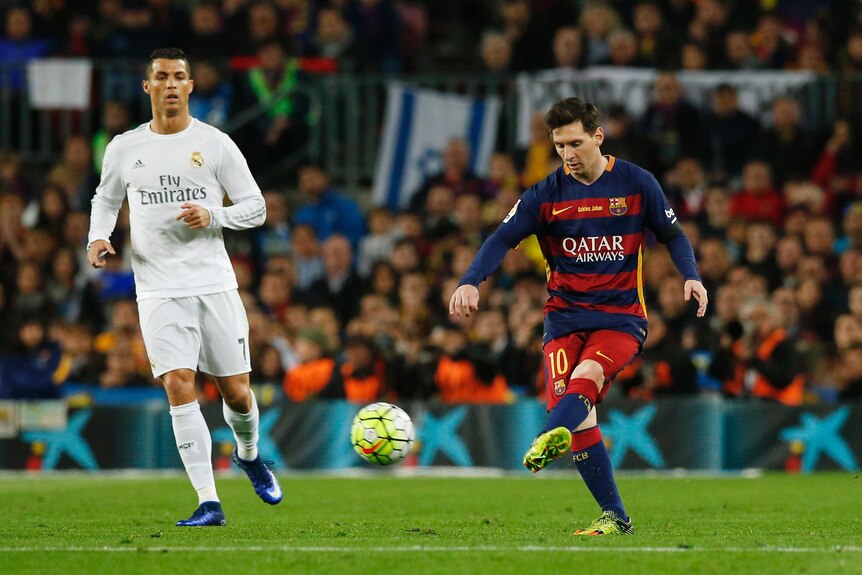 Lionel Messi passes the ball in front of Cristiano Ronaldo