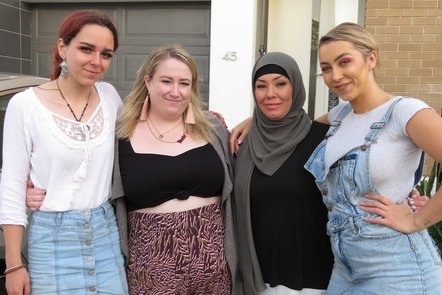 Four women, including comedian Rosie Waterland, stand with their arms around each other in front of a house.