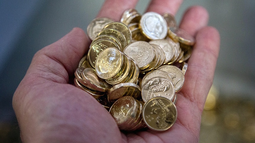 Shiny two dollar coins being held in the palm of a hand.