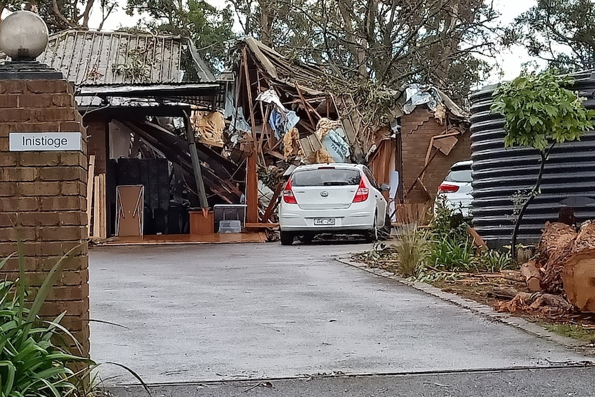 Une maison très endommagée avec des arbres tombés dessus.