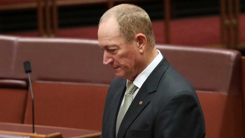 Fraser Anning, wearing a dark suit, bows his head while standing in the Senate.