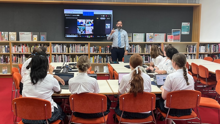 Matt stands by a large screen, which is showing AI-generated images. Students are seated at desks, looking at the screen.