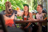 Four people sit at an outdoor table and cheers their drinks, surrounded by bikes and helmets. 
