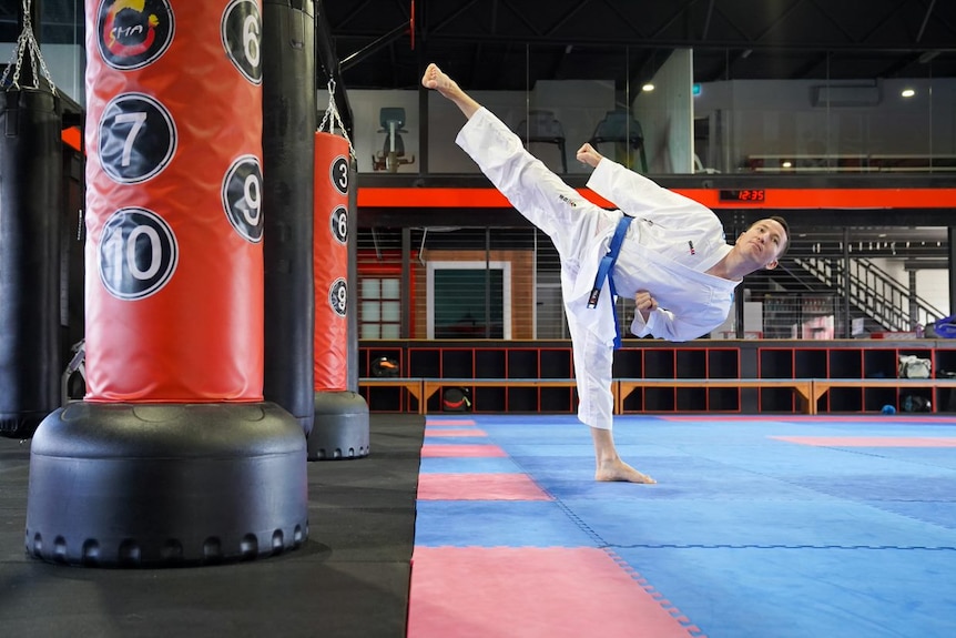 Man wearing a karate uniform doing a side kick in a dojo 