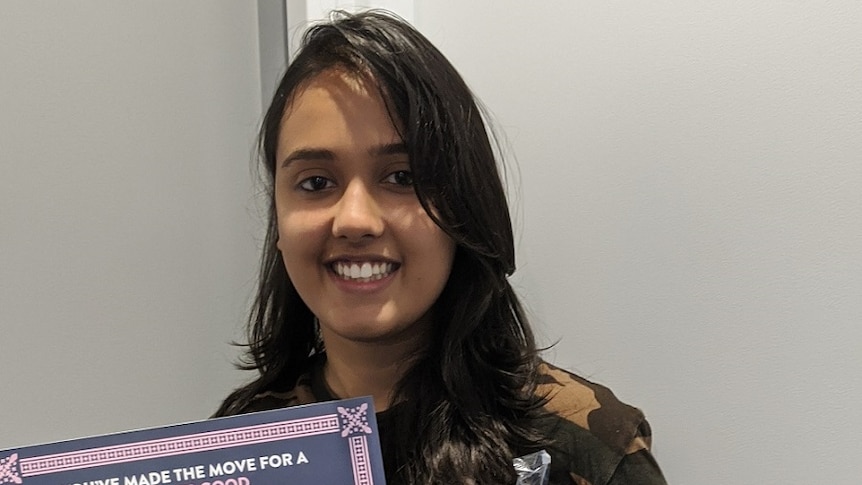 A photo of Sivangi Mund holding a certificate and a drink while she smiles at the camera.