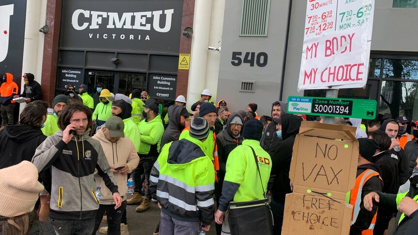 Building workers in a crowd with signs saying "no vax".