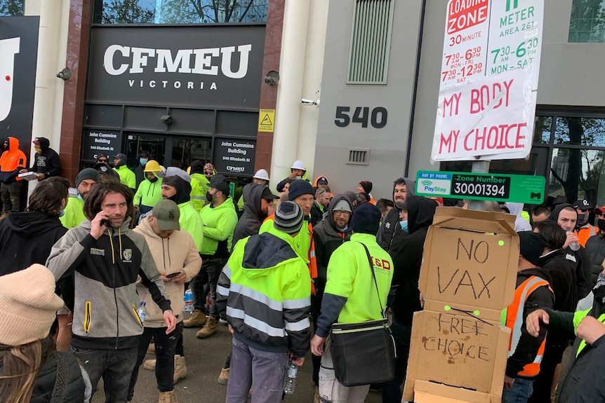 Building workers in a crowd with signs saying "no vax".