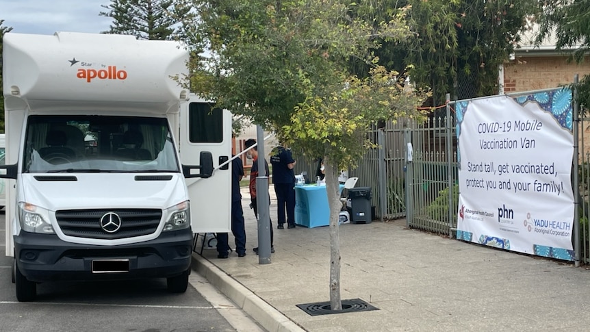 The front of a white mobile van with its side door open and health workers setting up a inside.