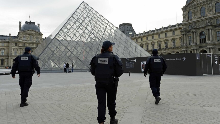 Police patrol in front of the Louvre Pyramid at the Louvre Museum in Paris.