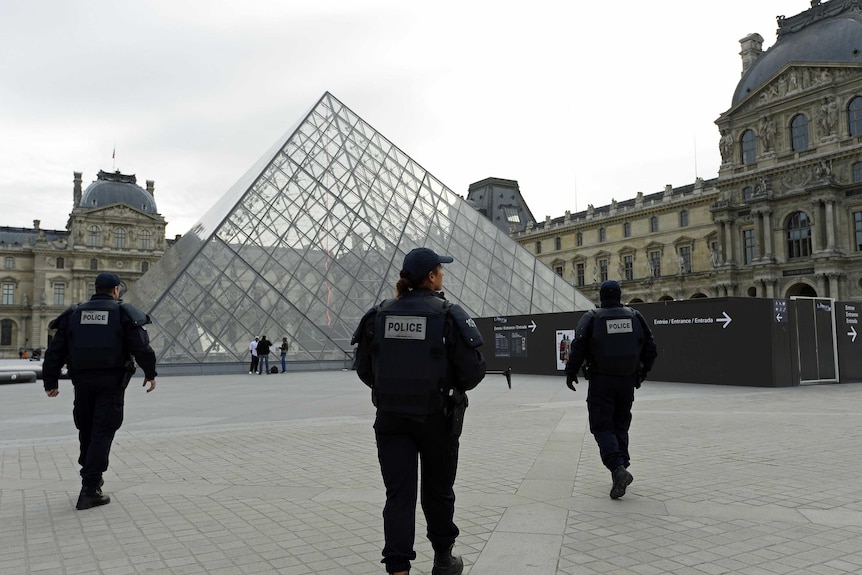 Police patrol in front of the Louvre Pyramid at the Louvre Museum in Paris.
