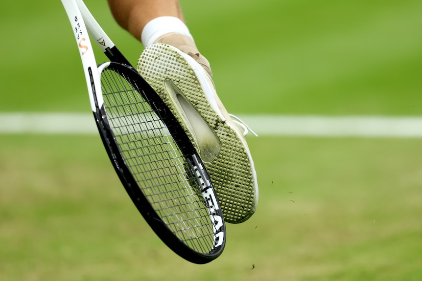 A tennis racquet hits the white shoe of a player on the grass court at Wimbledon.