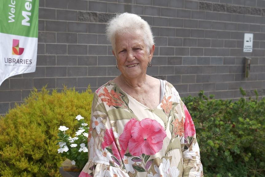 An elderly woman in a floral dress smiling out the front a local library in regional Victoria.