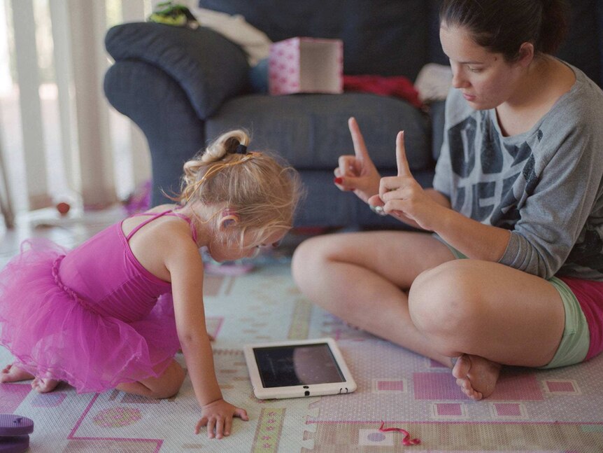 Amy Keating sits on the floor teaching her daughter Abbi sign language.