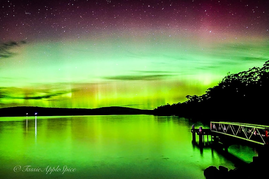 Pink and green lights of an Aurora Austalis over water 
