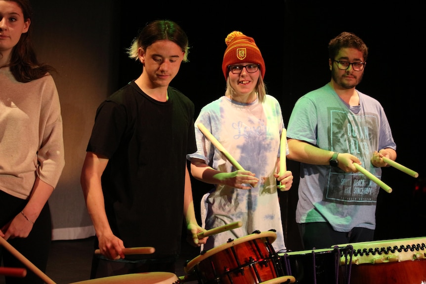 Four students standing in a row, holding drumsticks with drums in front of them. 