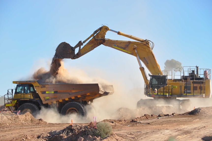 A digger dumps dirt into a haulpak on a mine site.