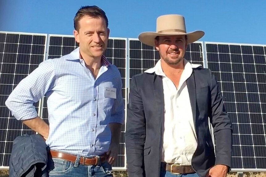 Two men stand in front of some solar panels near Longreach in 2018.