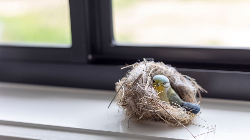 A trinket of a blue and yellow bird in a nest, sitting on a windowsill.