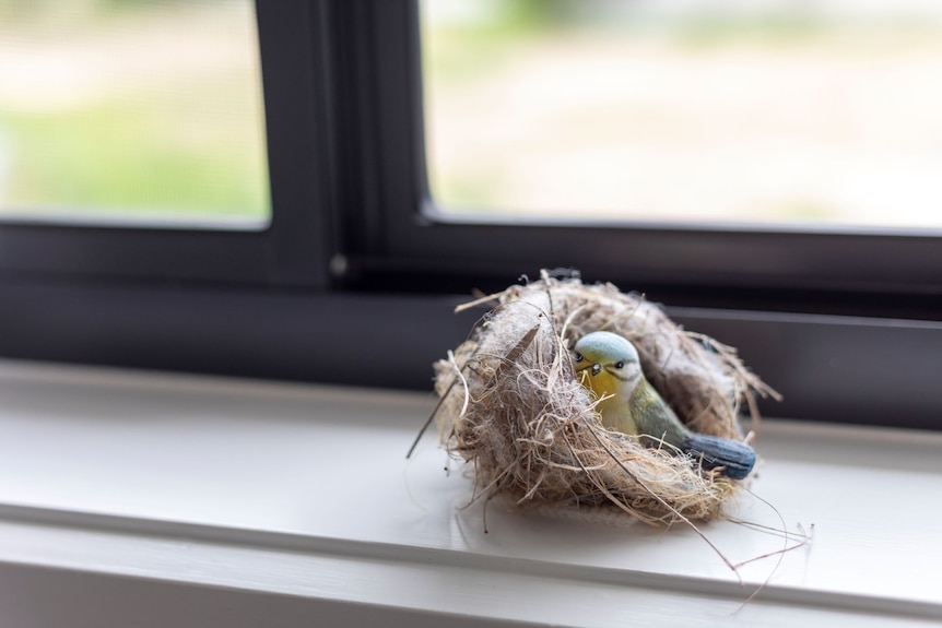 A trinket of a blue and yellow bird in a nest, sitting on a windowsill.