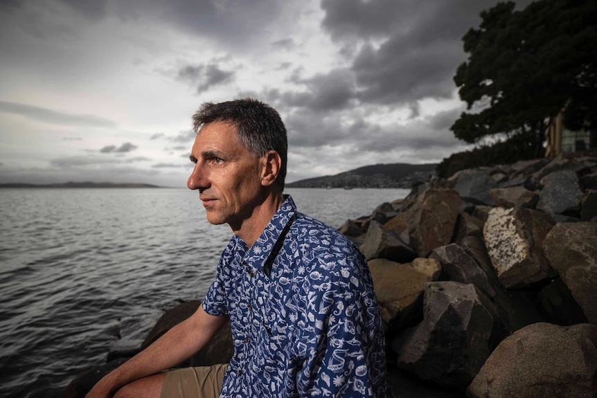 CSIRO oceans and atmosphere research scientist Dr Alistair Hobday sits on rocks beside ocean