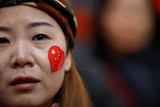 A close up of a woman's face with a heart-shaped sticker of the Chinese flag on her cheek.