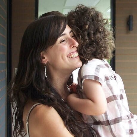 Helene a woman with long dark hair holds a young child in her arms, she is smiling