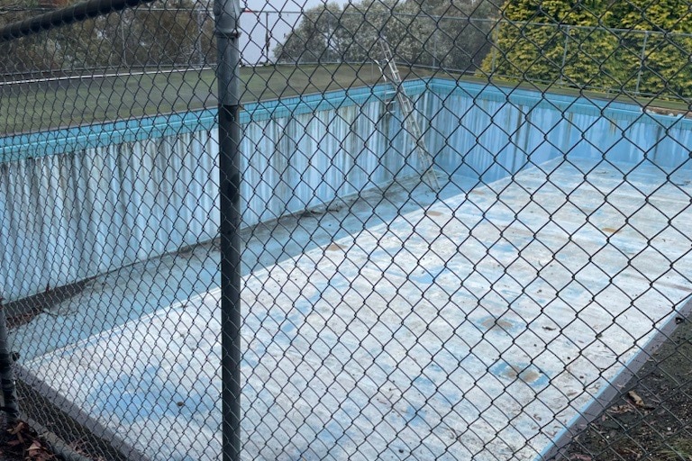 An empty pool surrounded by a chicken wire fence 