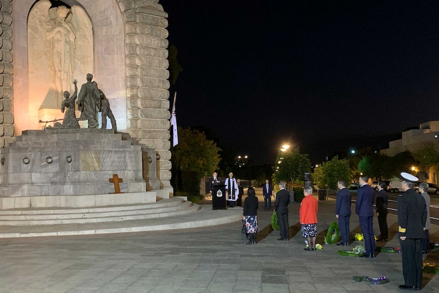 people lined up in front of a memorial with a lectern set up to the side