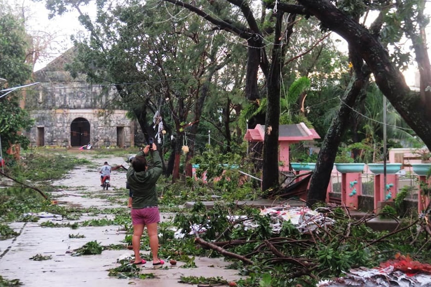 A debris-strewn street is pictured with branches littering a concrete street with a church building on the horizon.