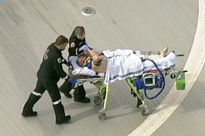 Tony Mokbel shakes hands with a paramedic as he is wheeled into hospital on a stretcher.