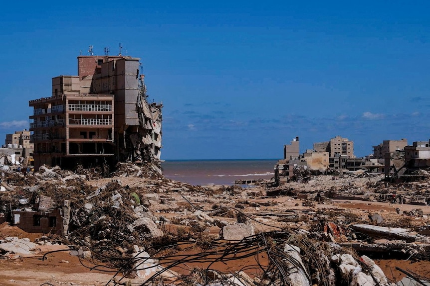 Destroyed buildings and ground covered in debris with the ocean showing behind them