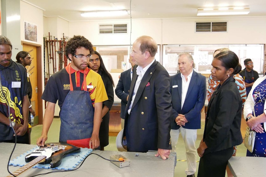 A Yirara College student wearing an apron talks to Prince Edward in a classroom, as the student takes apart a guitar.