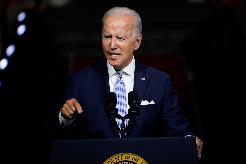 President Joe Biden stands at a lectern wearing a suit.  