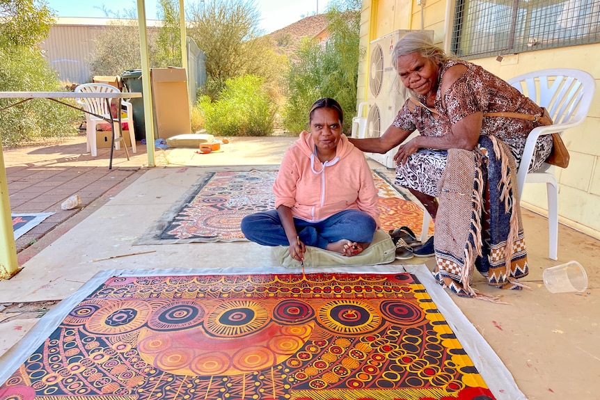 two women sit and paint on the ground