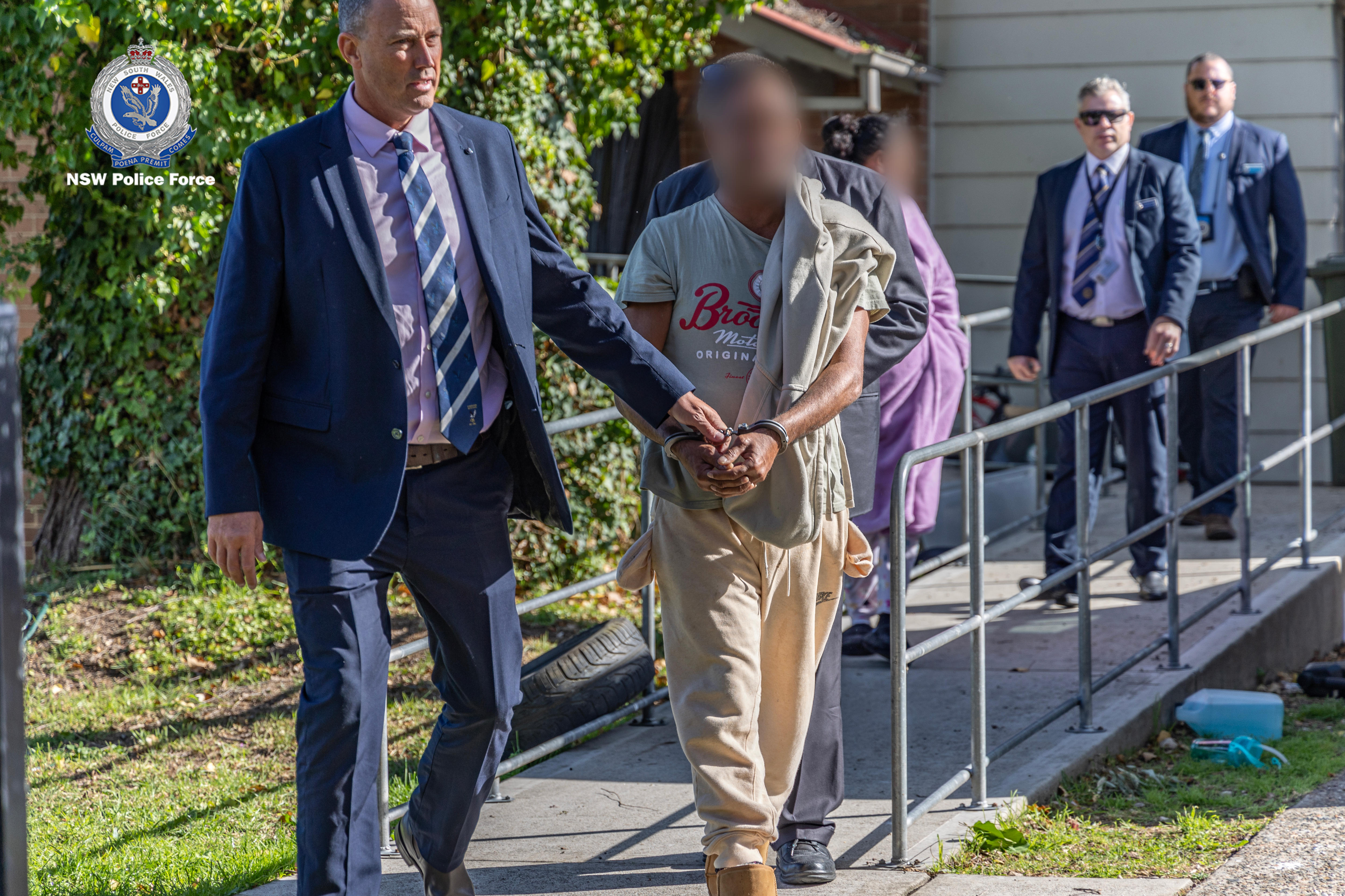 Police officers walk alongside anonymous man in handcuffs 