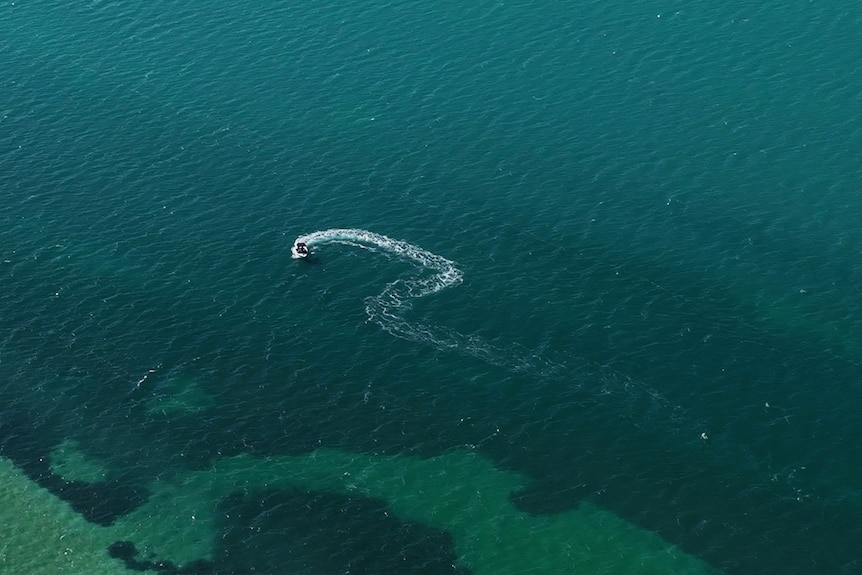 A boat makes a question mark shape in the water.