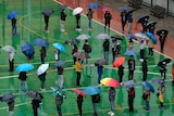 People with umbrellas line up on a court, while socially distancing. 