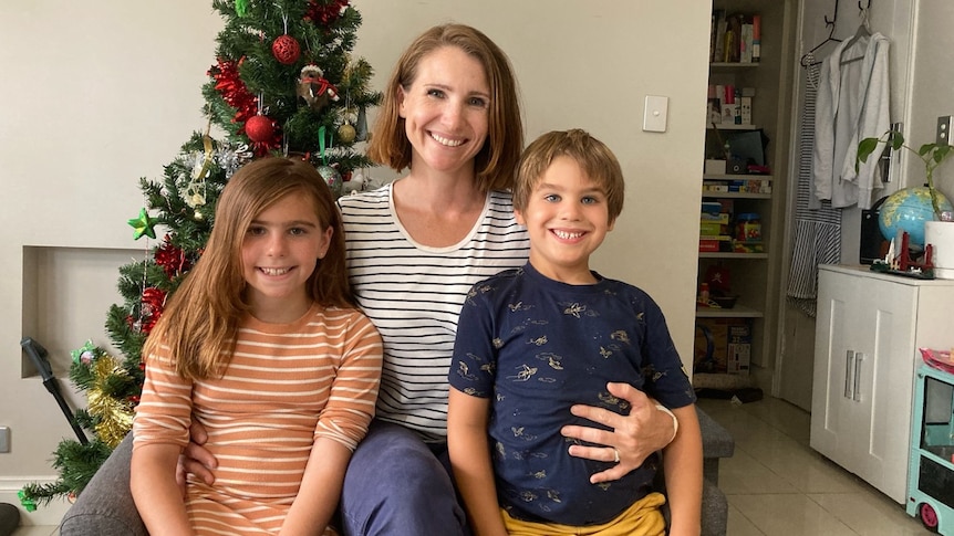 A woman with a girl and a boy sitting in front of a Christmas tree