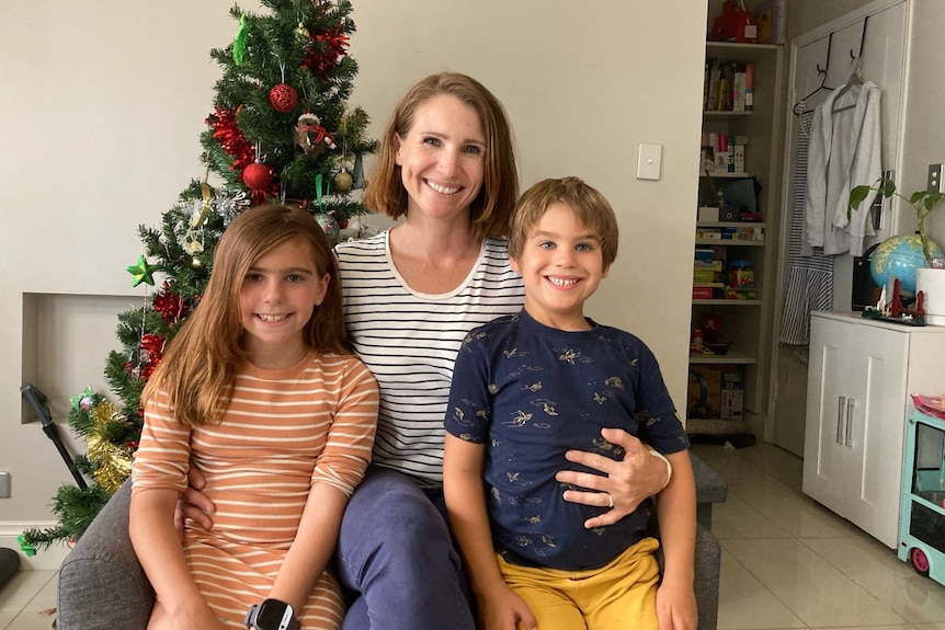 A woman with a girl and a boy sitting in front of a Christmas tree