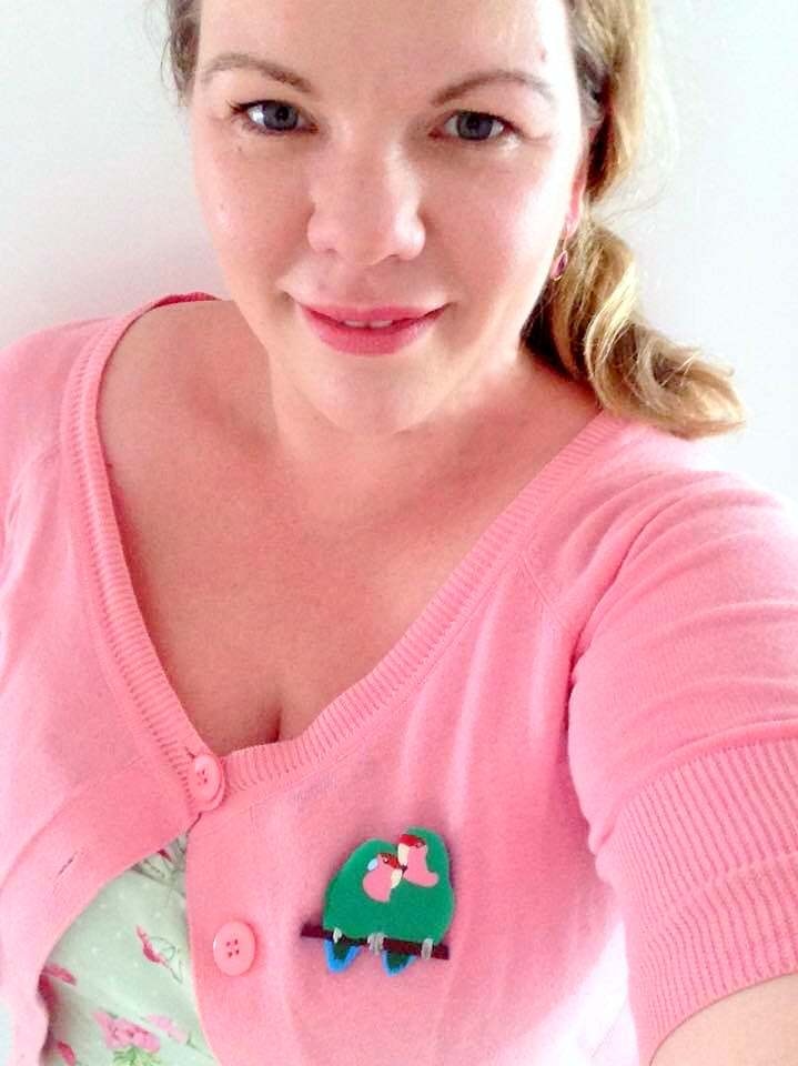 Woman with hair pulled back wearing pink top and a brooch