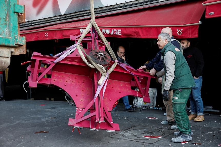 Red windmill sails that fell from the Moulin Rouge sing are lifted up by pieces of rope.