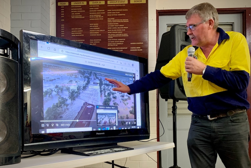 A man in hi vis points to a TV screen