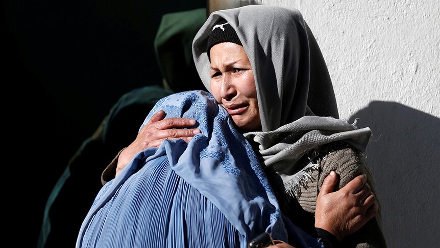 Two mourning Afghan women hold each other.