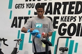 A man spraying an exercise bike with disinfectant in a gym